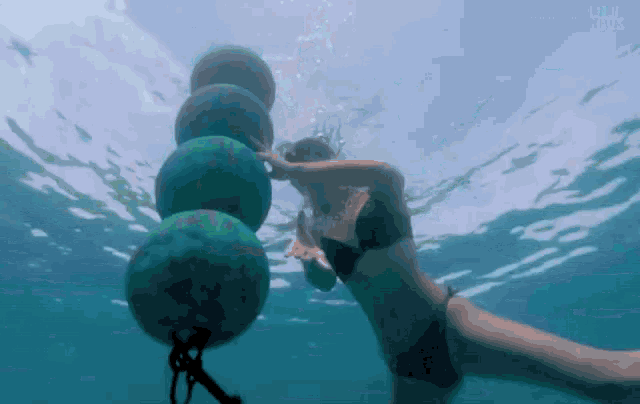 a woman in a bikini is swimming underwater with buoys