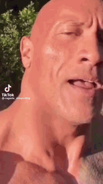 a bald man without a shirt is smoking a cigarette and making a funny face .