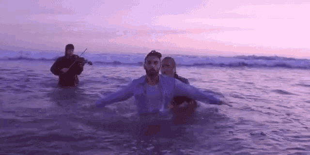 a man in a blue shirt is standing in the ocean while another man plays violin
