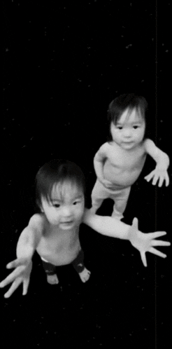 a black and white photo of two babies standing next to each other .