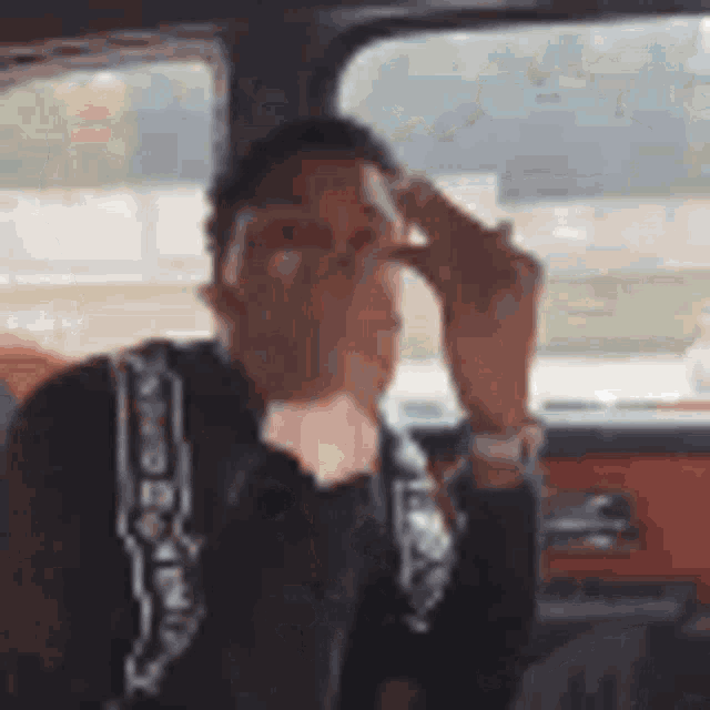 a man is sitting in the driver 's seat of a car covering his face with his hand .