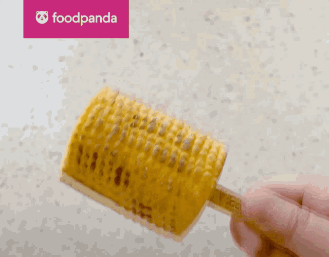 a person is holding a piece of corn on the cob with a foodpanda logo in the background