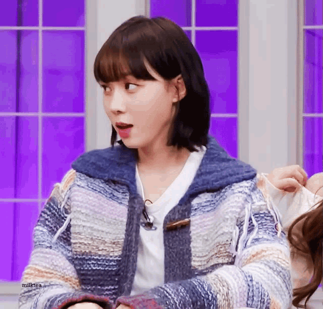 a woman wearing a blue and white striped sweater is sitting in front of a purple window .