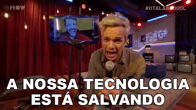 a man holding a microphone in front of a screen that says a nossa tecnologia esta salvando