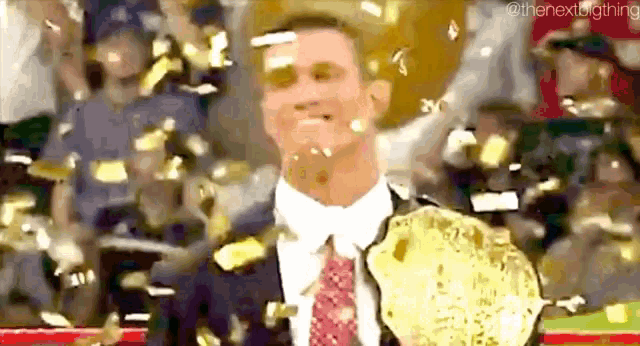 a man in a suit and tie is holding a wrestling championship belt while confetti is falling on him .