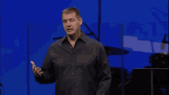 a man in a black shirt is standing in front of a blue screen .