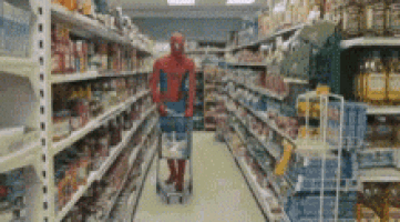 a man in a spiderman suit is pushing a shopping cart through a grocery store aisle .
