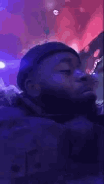 a man with a beard is smoking a cigarette in a dark room with purple lights .