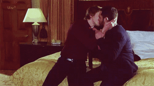 two men kissing on a bed in front of a tv screen that says itv