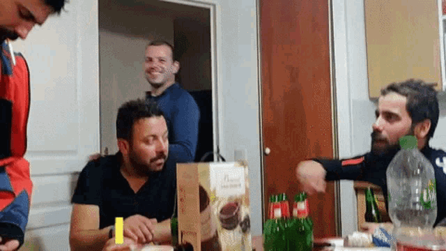 a group of men are sitting around a table with bottles of beer and a box of french vanilla