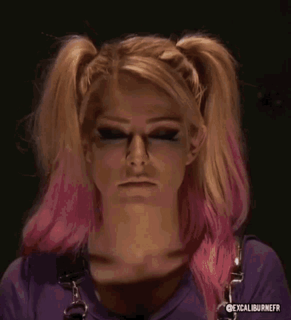 a woman with pigtails and pink hair is making a funny face while wearing a purple shirt .