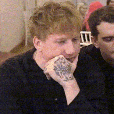 a man with a tattoo on his wrist is sitting at a table .
