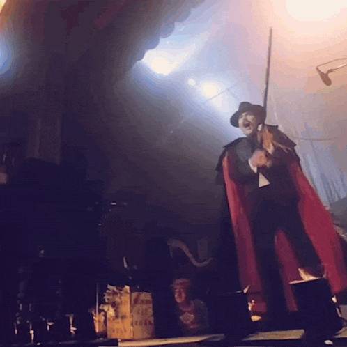 a man in a red cape is standing on a stage holding a sword