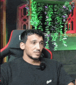a man sitting in a chair with a microphone on his neck and a black shirt that says ' lacoste ' on it