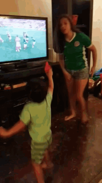 a girl in a green shirt is standing in front of a tv