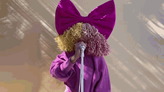 a woman wearing a purple wig and a purple bow holds a microphone