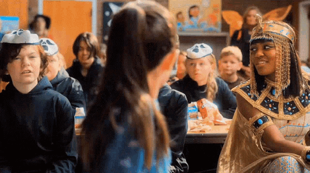 a girl in a costume is talking to another girl in a classroom