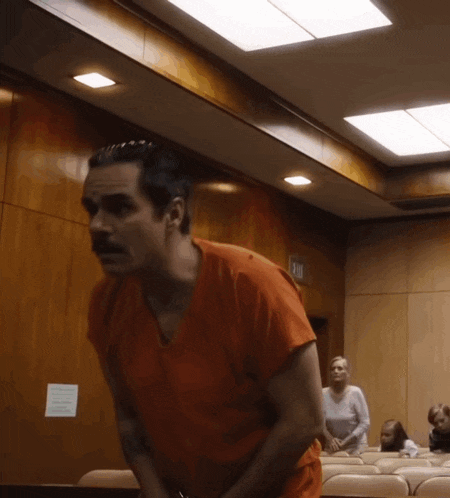 a man in an orange shirt stands in a courtroom