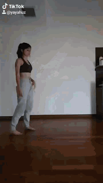 a woman is standing on a wooden floor in a room with a white wall .
