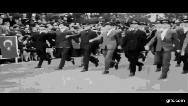 a black and white photo of a group of men in suits and hats running in a parade .