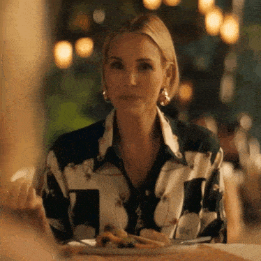 a woman in a floral shirt is sitting at a table with a plate of food in front of her .