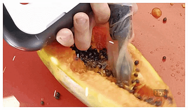 a person is cutting a papaya with a knife on a cutting board with a tbs logo in the background