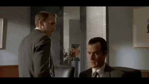 two men in suits and ties are standing next to each other in an office .