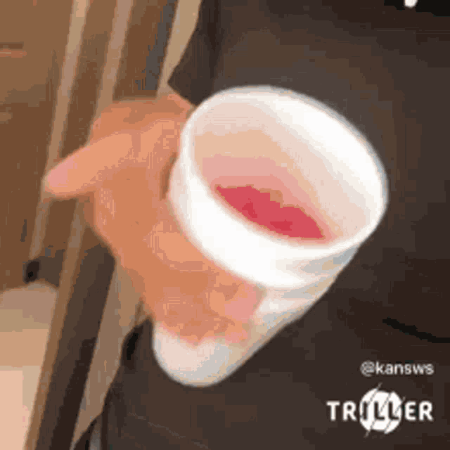 a person is holding a cup of red liquid .