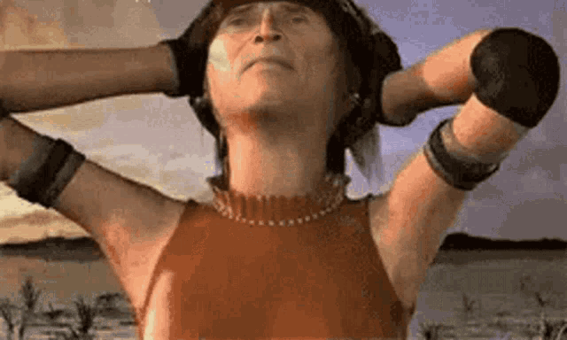 a woman is standing in the desert with her arms outstretched and her hands behind her head .