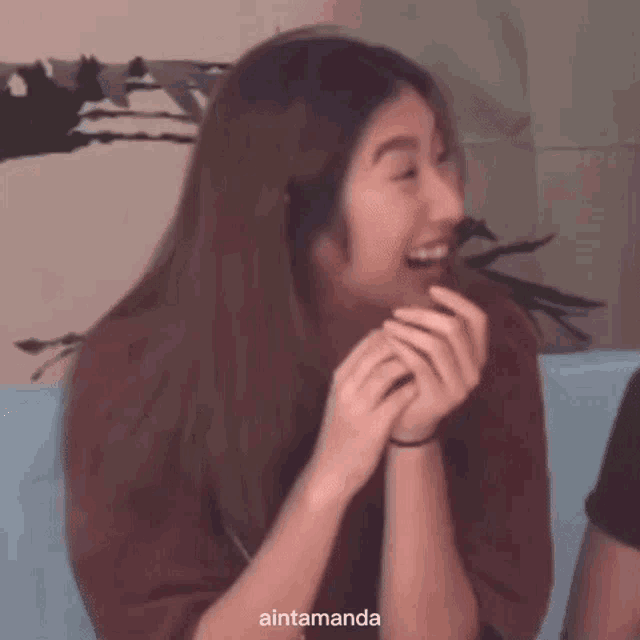 a woman is laughing while sitting on a couch with her hands folded .
