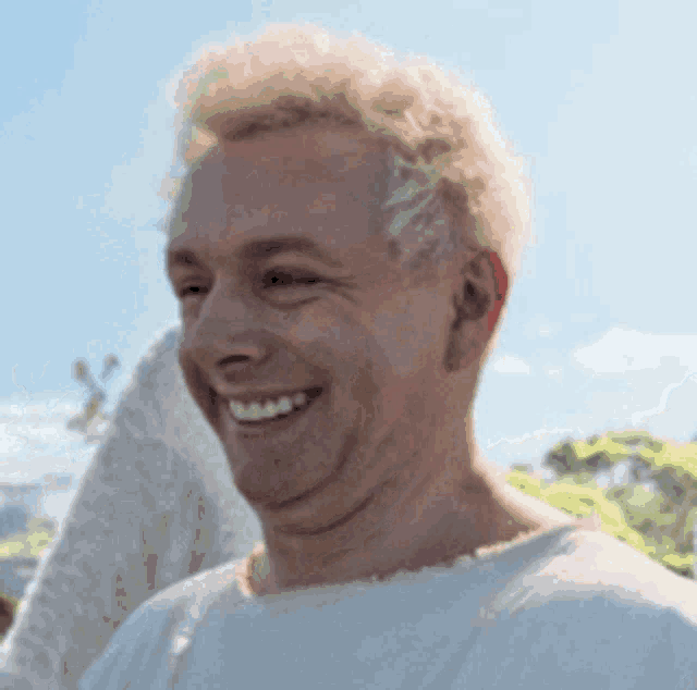 a man with blonde hair is smiling for the camera while wearing a white shirt .
