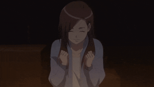 a woman with long brown hair is sitting in a dark room with her fists in the air