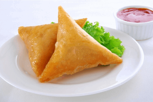 a white plate topped with two fried triangles next to a small bowl of ketchup