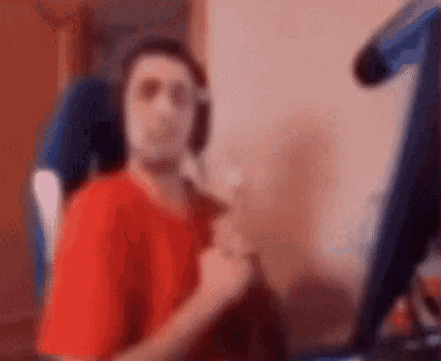 a man in a red shirt is sitting in front of a computer monitor .