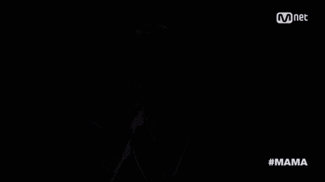 a man in a suit and tie stands on a stage with a mnet logo behind him