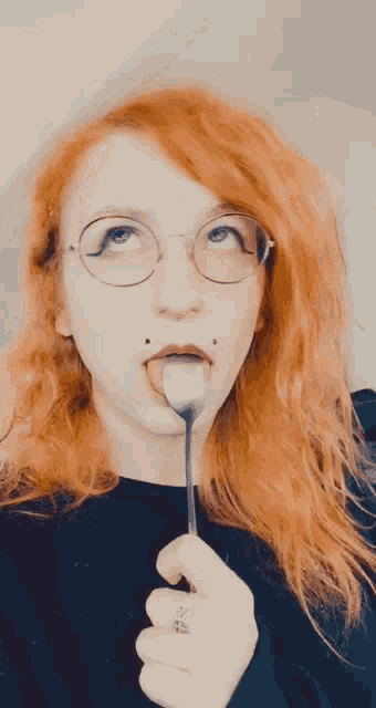 a woman with red hair and glasses is holding a fork in her mouth and sticking it out .