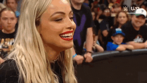 a woman is smiling in front of a crowd of people in a wrestling ring .