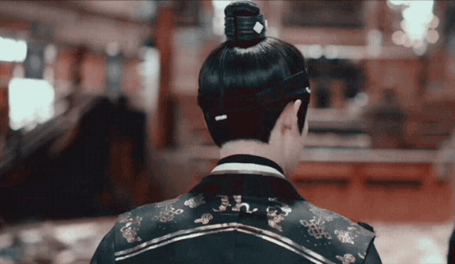 a man with a bun on his head wears a black and gold jacket