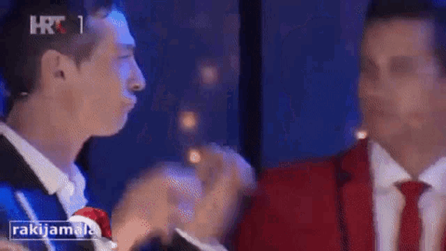 two men in suits and ties are clapping in front of a sign that says rakijama