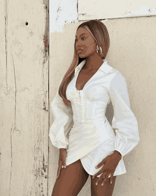 a woman wearing a white dress and hoop earrings stands in front of a white wall