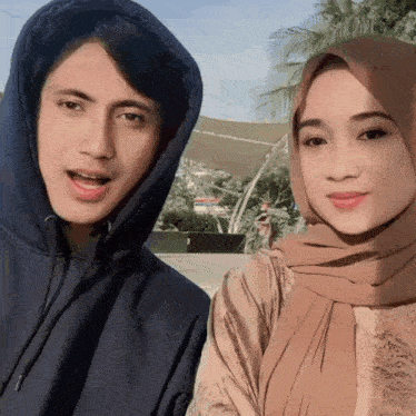 a man in a hoodie and a woman in a hijab pose for a photo
