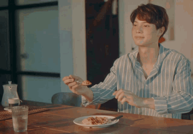 a man in a striped shirt is sitting at a table with a plate of food
