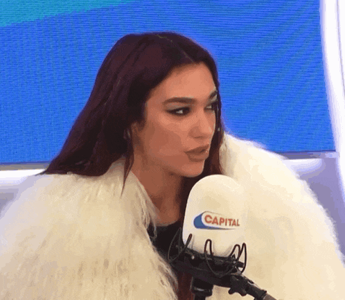 a woman in a fur coat is sitting in front of a capital radio microphone .