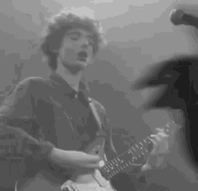 a man with curly hair is playing a guitar and singing into a microphone .