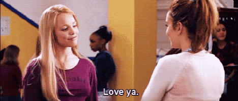 two women are standing next to each other in a hallway talking to each other .