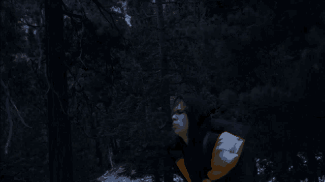 a man in a black and yellow jacket is walking through a forest