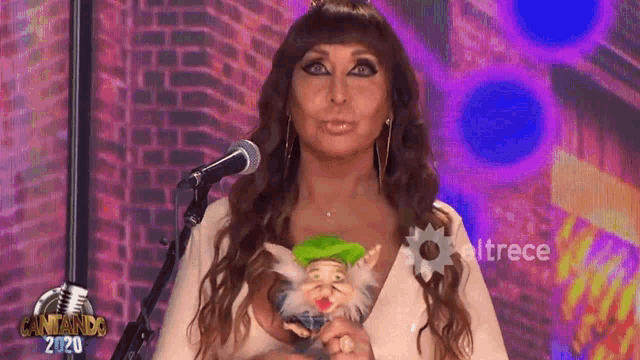 a woman is holding a puppet in front of a microphone and the words cantando 2020 are on the bottom