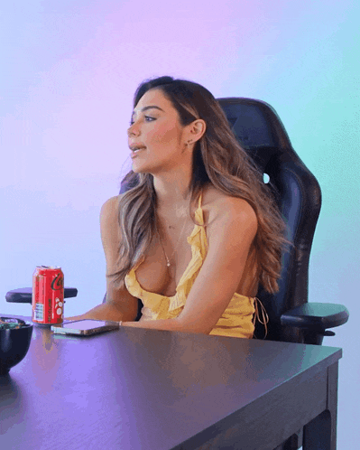 a woman in a yellow dress sits at a desk with a coke can on it