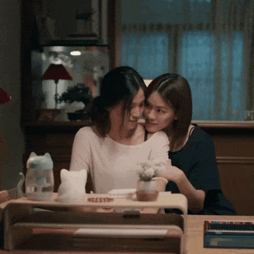 two women are hugging each other in front of a desk with a cat on it that says ' sleep '