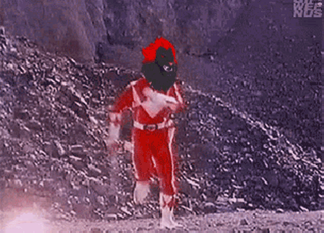 a red power ranger with a christmas hat on his head is walking on a rocky hillside .